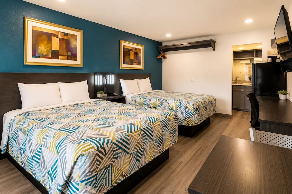 A hotel room with two beds, a desk, a chair, a TV, and artwork on the walls.