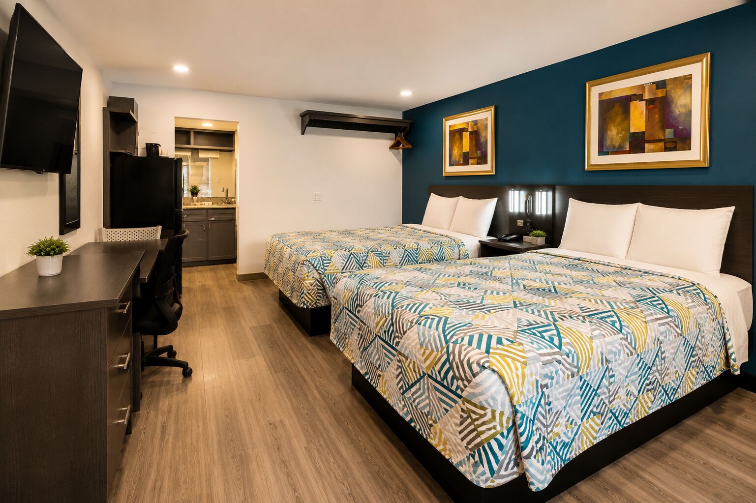 A hotel room with two beds, a desk, a TV, and artwork on the walls.