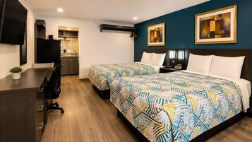 A hotel room with two beds, a desk, a TV, and artwork on the walls.