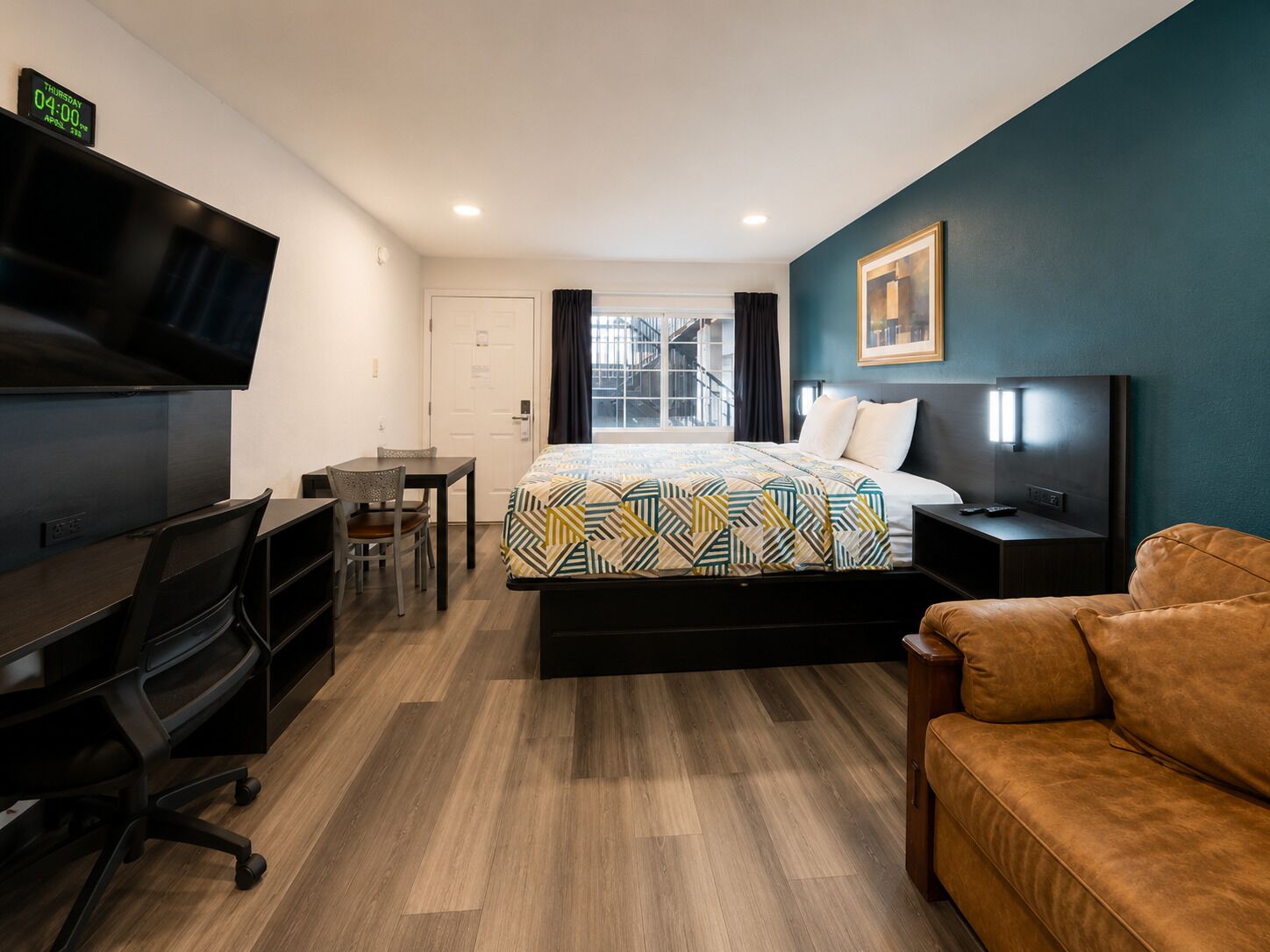 A hotel room with a bed, desk, chair, TV, and a couch.