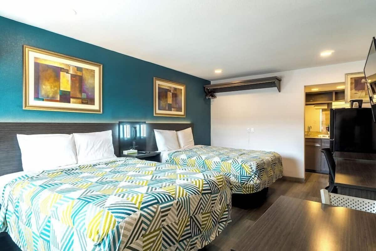A hotel room with two beds, a desk, a chair, and a kitchenette.
