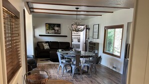 A spacious living room with a dark-colored sofa, a dining table with chairs, and a chandelier.