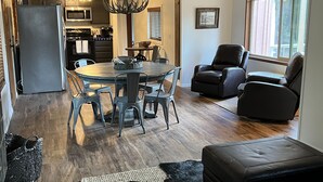A modern kitchen with a dining area, including a chandelier, a dining table with chairs, and a leather sofa.