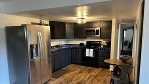 A modern kitchen with dark cabinets, stainless steel appliances, a wooden floor, and a dining area with a table and chairs.