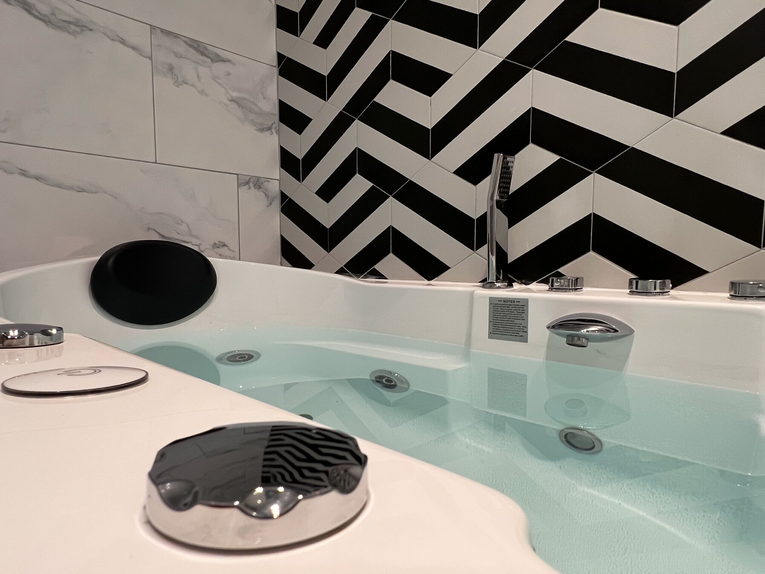 Een moderne badkamer met een vrijstaand bad, een zwart, rond voorwerp op het aanrecht en een wand met een zwart-wit ruitpatroon.