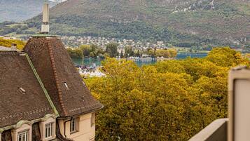 Een gebouw met een schuin dak en schoorsteen, met uitzicht op een stad en een meer met bergen op de achtergrond.