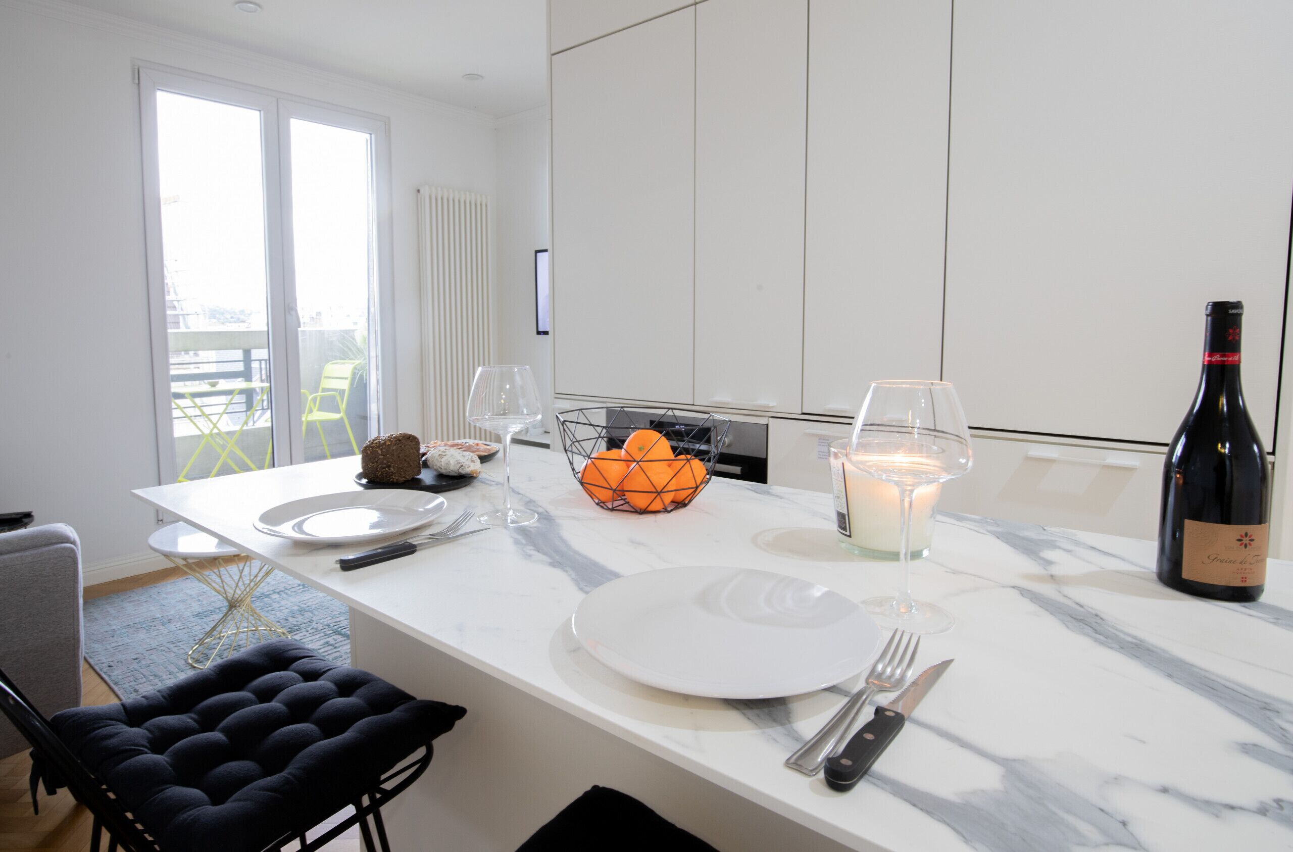 Een moderne keuken met een marmeren aanrecht, een gedekte eettafel met borden, bestek en een kaars.