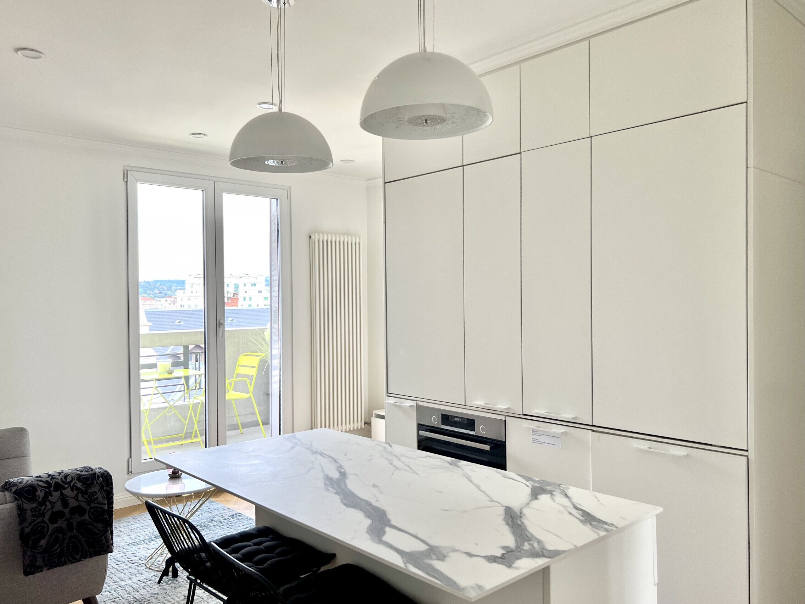 Een moderne keuken met witte kastjes, een marmeren aanrechtblad en hangende lampen.