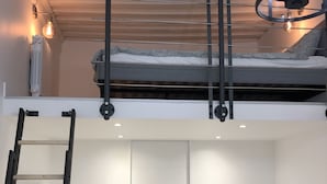 Et loft-agtigt soveværelse med køjeseng, stige, sofa og skrivebord.