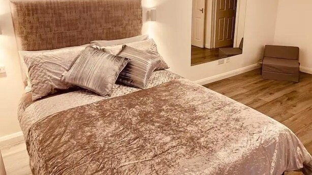 Une chambre à coucher avec un lit, des oreillers, une table de chevet, un miroir et un plancher en bois.