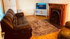 Un salon avec un canapé en cuir noir, un meuble de rangement blanc sur lequel est posée une télévision affichant le logo « NETFLIX », une cheminée et un buffet blanc.
