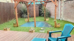Une terrasse en bois avec une pergola, une petite piscine et deux chaises bleues.