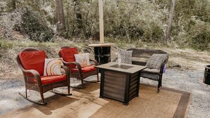 An outdoor seating area with wicker chairs and a table, surrounded by a natural forest setting. - The Pendle-Tin (Pendleton)