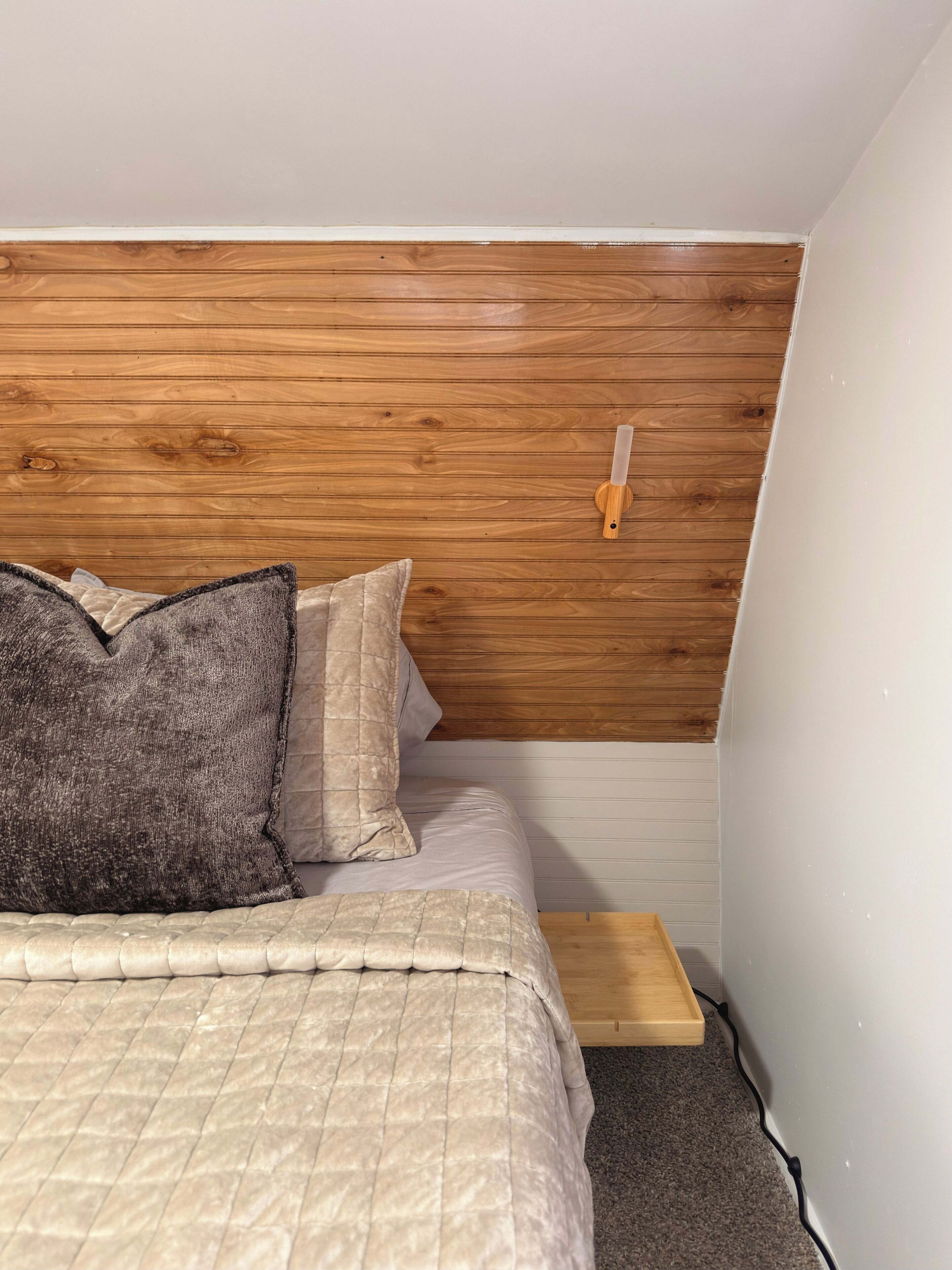 Ein Schlafzimmer mit einem hölzernen Kopfteil, einem Bett mit einer beige farbenen Tagesdecke und einem Nachttisch.