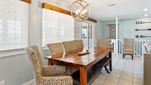 A dining area with a wooden table and wicker chairs, a chandelier, and a view of the outside. - Spacious Beachside Home with Private Pool! Dog-Friendly & Directly Across from Beach! (South Padre Island)