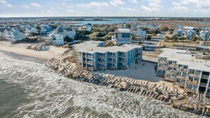 Zona residencial costeira com propriedades à beira-mar, incluindo edifícios de vários andares com varandas, localizada perto de uma praia de areia e do oceano.