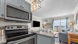 Cozinha moderna equipada com micro-ondas, forno e fogão. Dispõe de área de jantar com mesa e cadeiras, e varanda com vista para o mar.
