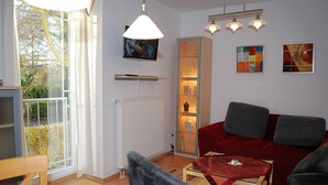 A living room with a red sofa, a glass cabinet, a television, and a window with curtains.