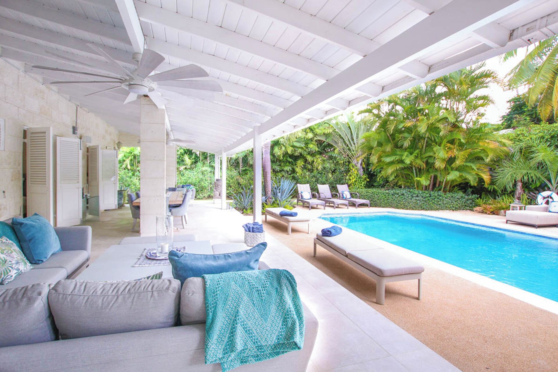 A covered outdoor area with a pool, lounge chairs, and a sofa with cushions.
