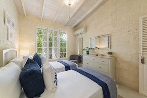 A bedroom with two beds, a dresser, a chair, and a window with a view of greenery.