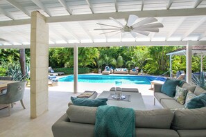 An outdoor seating area with a pool, lounge chairs, and a ceiling fan.