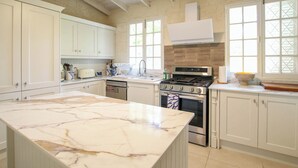 Una cocina con armarios blancos, encimera de mármol, estufa y lavavajillas.
