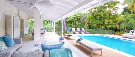 Un espacio al aire libre cubierto con piscina, sillones de descanso y un sofá con cojines.