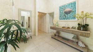 Un pasillo con pared de piedra, un espejo, una obra de arte enmarcada de una tortuga marina, una consola decorativa con objetos ornamentales y una planta en maceta.