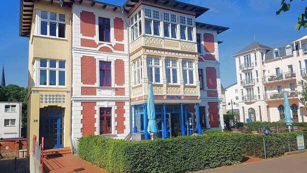 En bygning i flere etager med forskellige arkitektoniske stilarter, herunder en del med detaljeret udsmykning og en anden med en mere enkel facade.