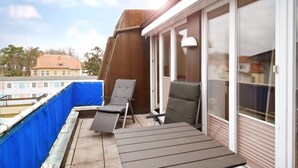 Un balcon avec deux fauteuils et une table, donnant sur une étendue d’eau et des bâtiments.