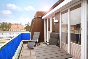 Ein Balkon mit zwei Lounge-Stühlen und einem Tisch, mit Blick auf ein Gewässer und Gebäude.