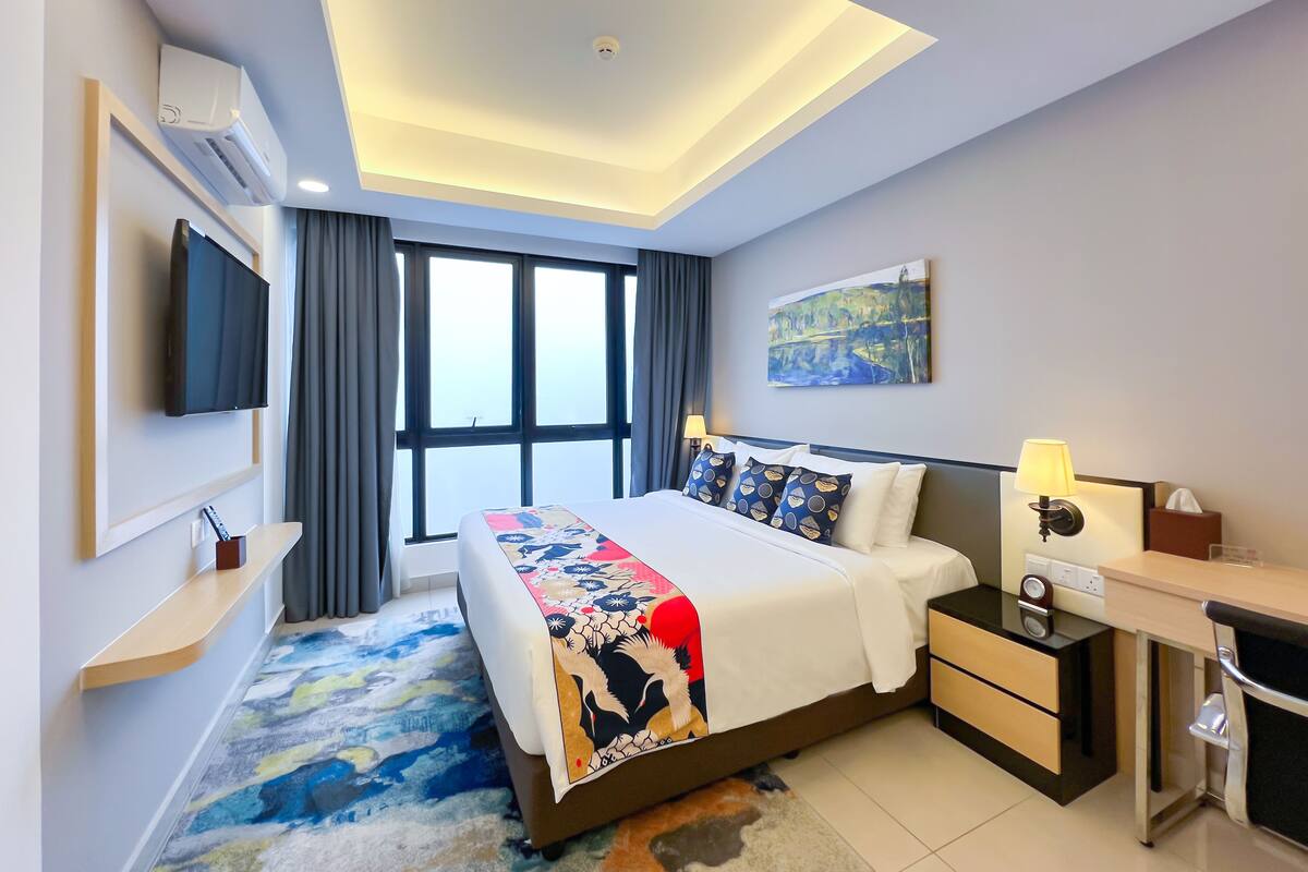Une chambre d’hôtel moderne avec un grand lit, un bureau avec une lampe, un téléviseur à écran plat et un tableau au mur.