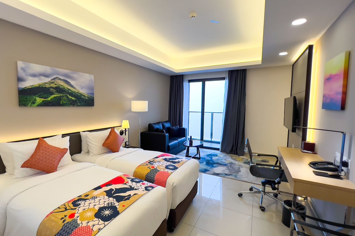 Une chambre d’hôtel avec deux lits, un bureau, une chaise, une télévision et une grande fenêtre.