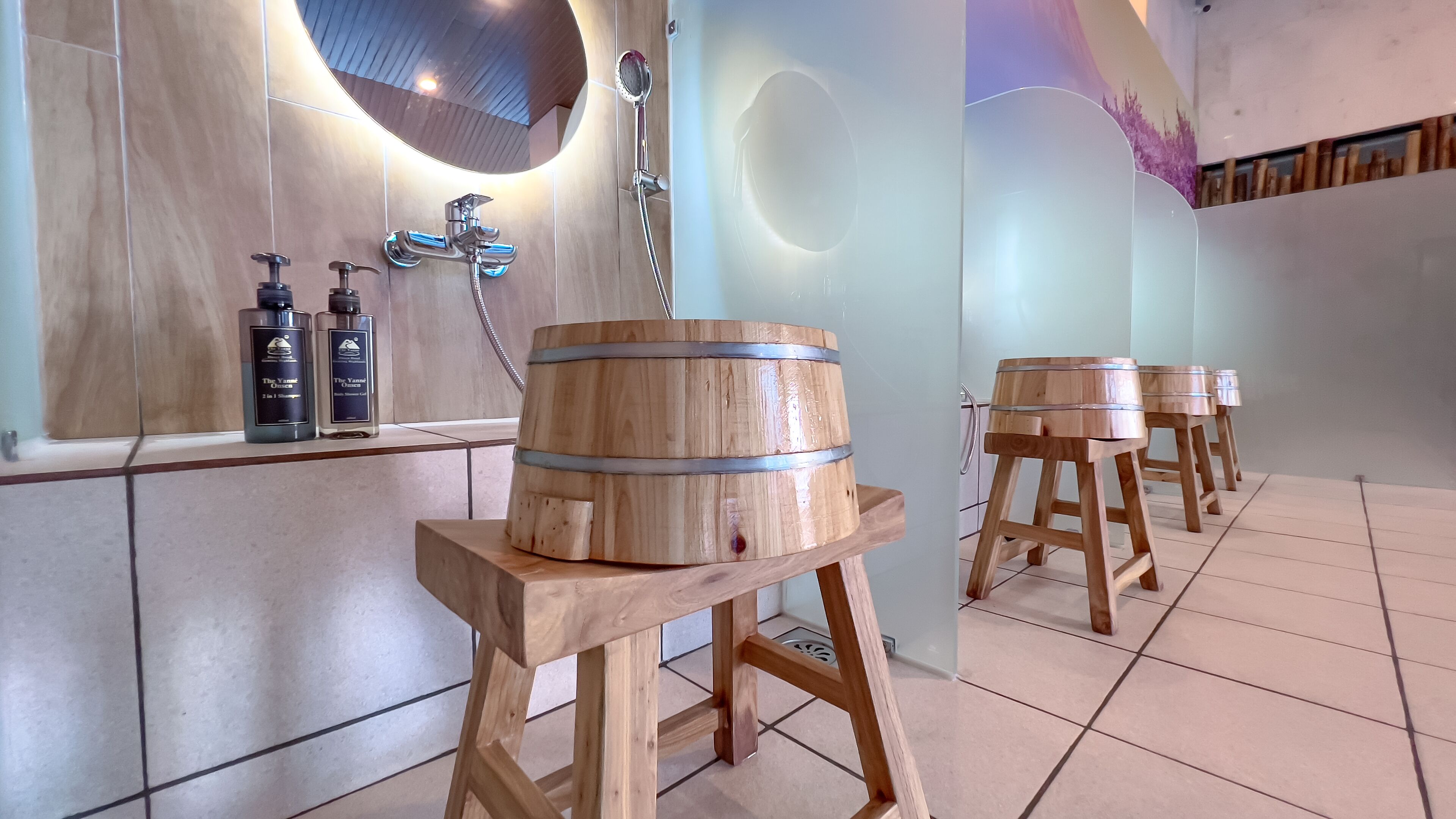 A bathroom with wooden barrels as stools, a mirror, and two bottles of The Yancey Onsen on the counter.