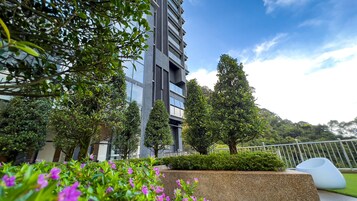 A modern building with balconies, surrounded by lush greenery and a clear sky.