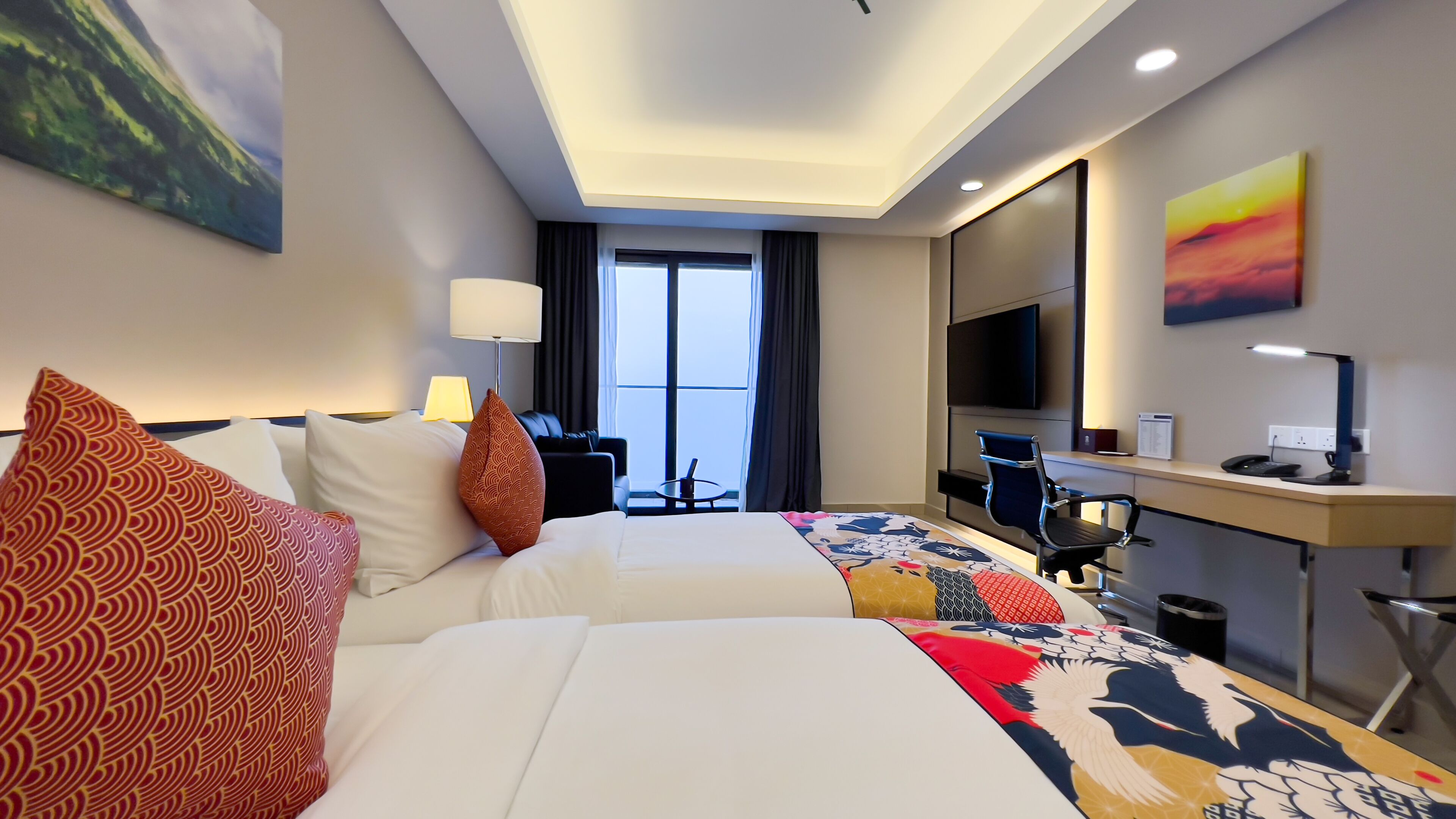 Habitación de hotel con dos camas, un escritorio con ordenador, televisor y ventana con cortinas.