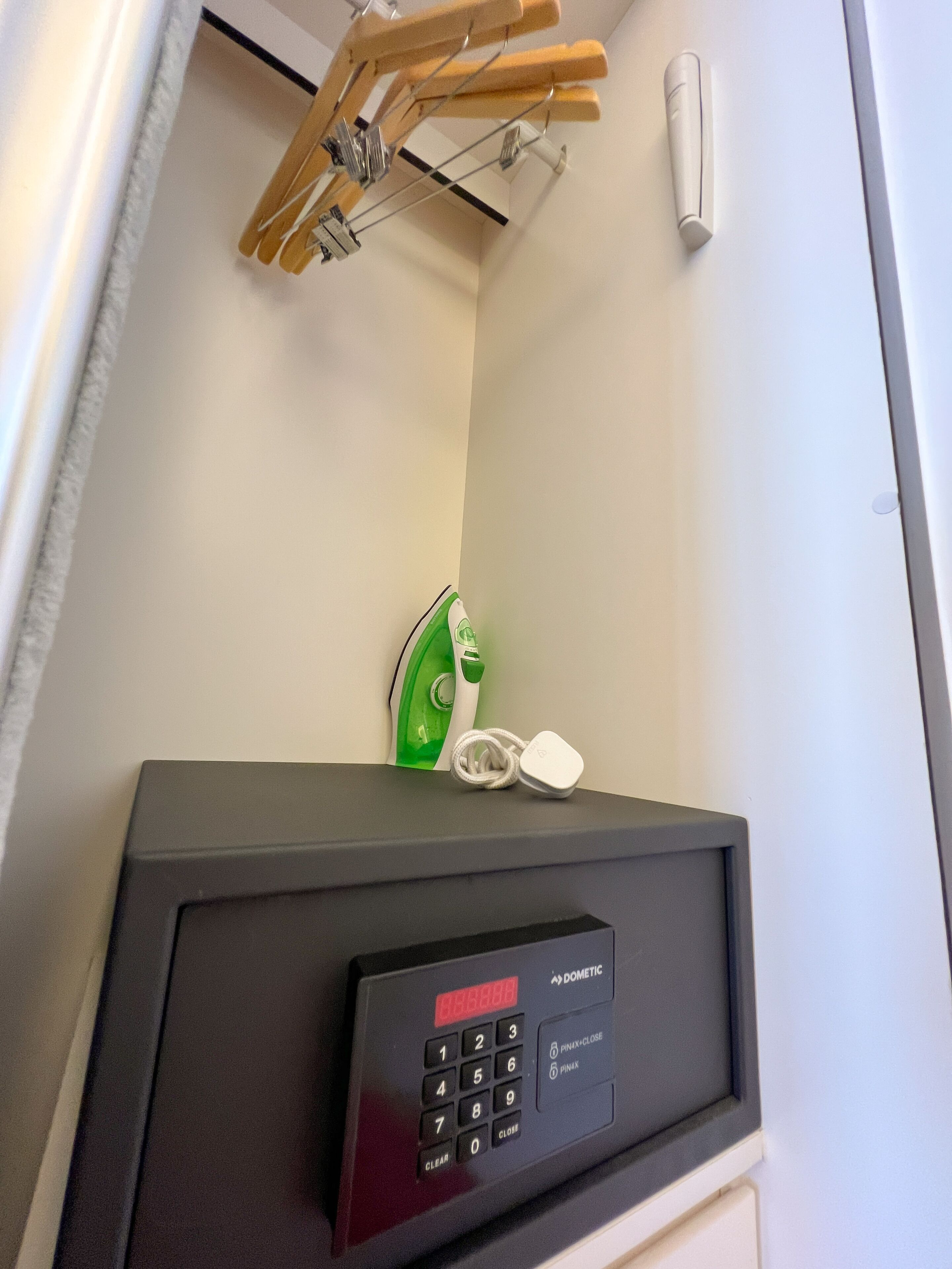 A room with a black safe, a green iron, and wooden hangers on a wall-mounted rack.