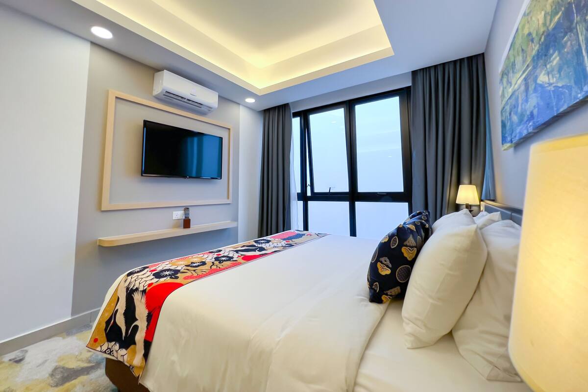 Une chambre d’hôtel moderne dotée d’un grand lit, d’un téléviseur à écran plat, d’un système de climatisation, d’une fenêtre avec des rideaux et d’un tableau au mur.
