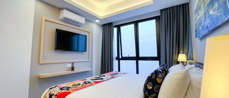 A modern hotel room with a large bed, a flat-screen TV, an air conditioning unit, a window with curtains, and a painting on the wall.