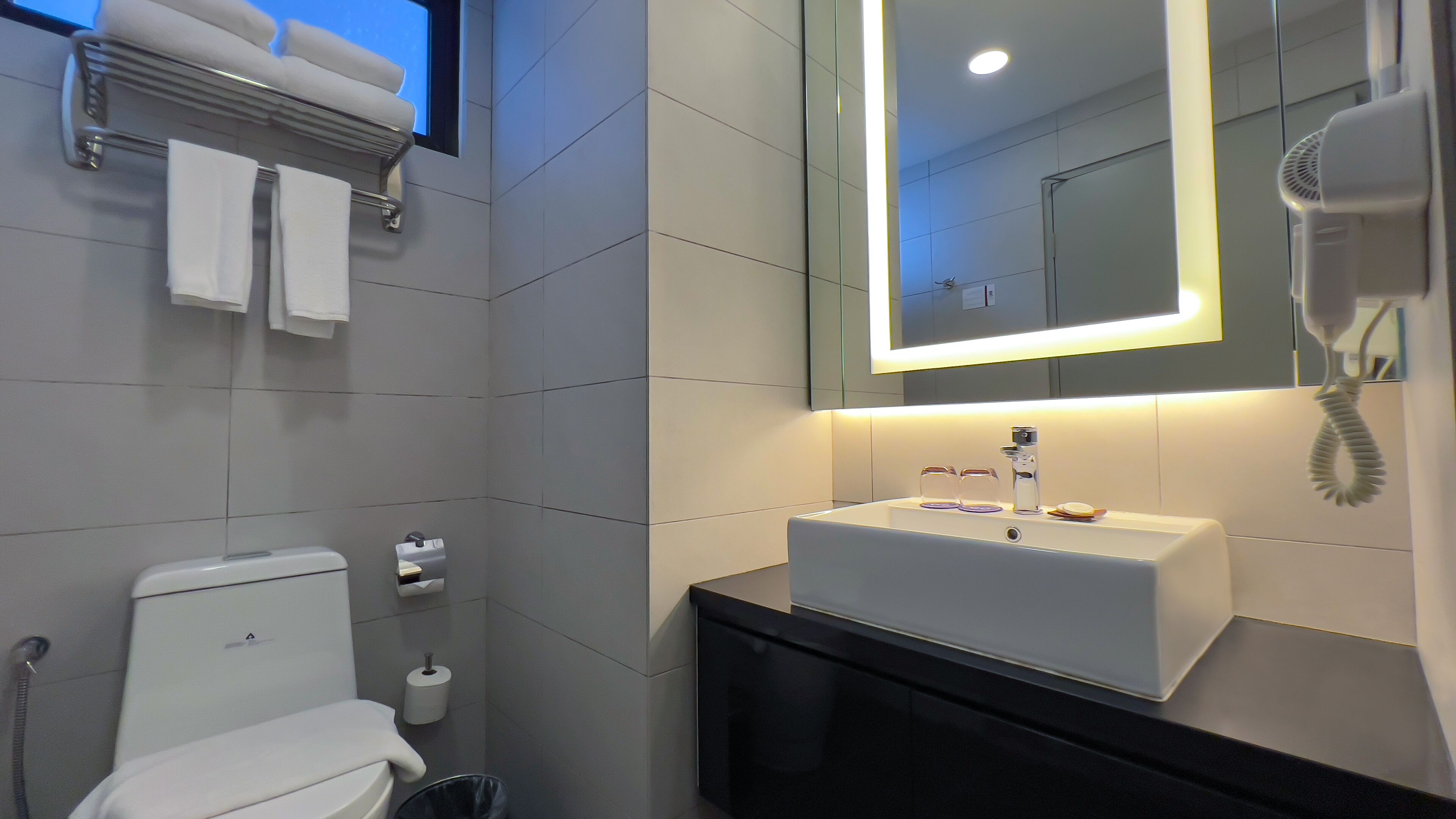 A modern bathroom with a white toilet, a sink with a mirror above it, and a hairdryer on the wall.