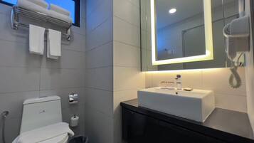 A modern bathroom with a white toilet, a sink with a mirror above it, and a hairdryer on the wall.