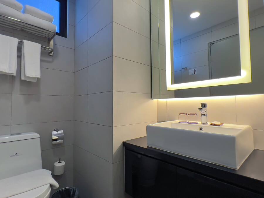 A modern bathroom with a white toilet, a sink with a mirror above it, and a hairdryer on the wall.