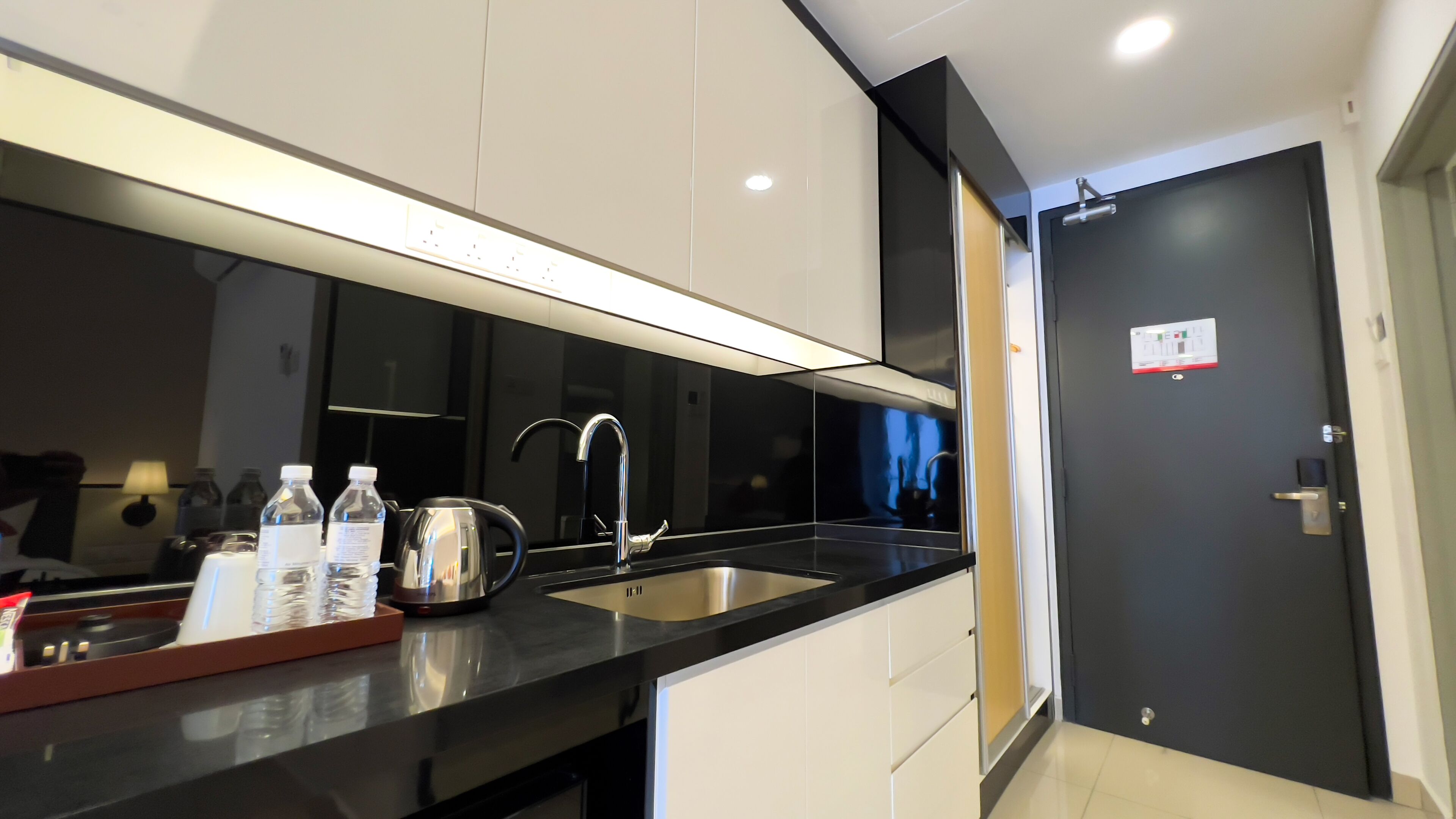 A modern kitchen with a black countertop, stainless steel sink, and white cabinets. There is a kettle and water bottles on the counter.