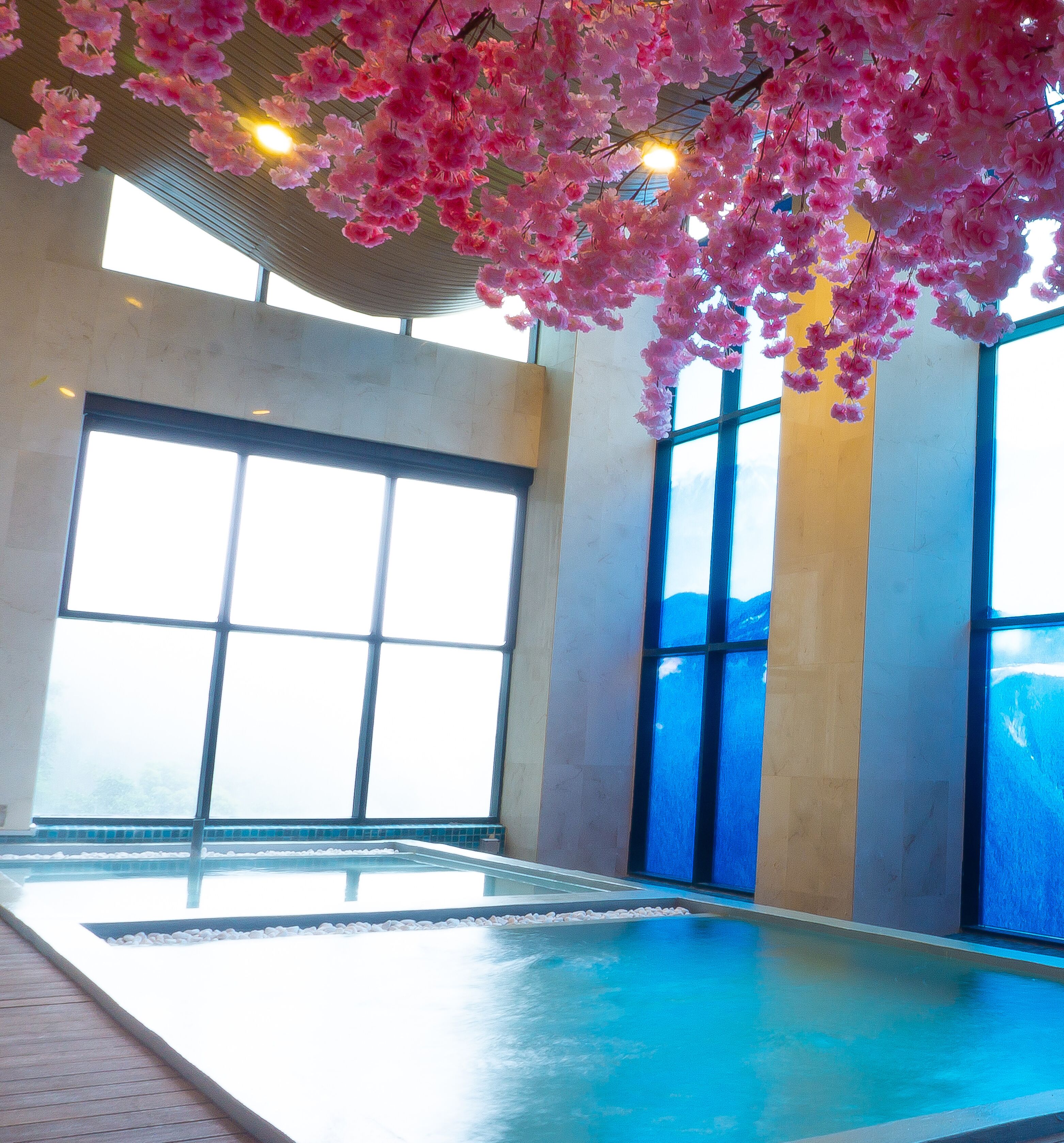 Une piscine intérieure dotée de grandes fenêtres, d’un plafond orné de motifs floraux roses et offrant une vue sur les montagnes.