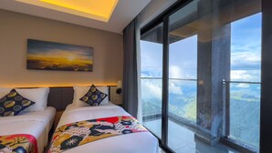 Een hotelkamer met een groot raam, met uitzicht op de lucht en wolken. Er staan twee bedden met kussens en een deken.