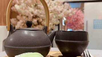 A tea set with a teapot and cups on a wooden table, accompanied by a plate with a green tea bag and cookies.
