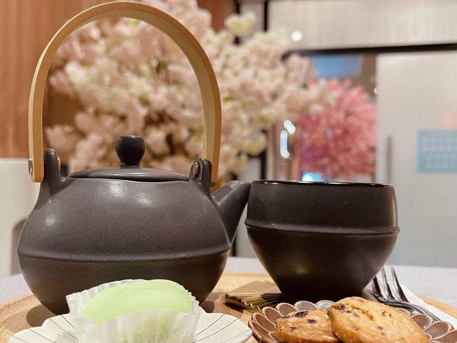 A tea set with a teapot and cups on a wooden table, accompanied by a plate with a green tea bag and cookies.