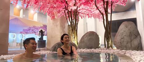 A hot spring area with pink cherry blossoms, large rocks, and a modern interior design.