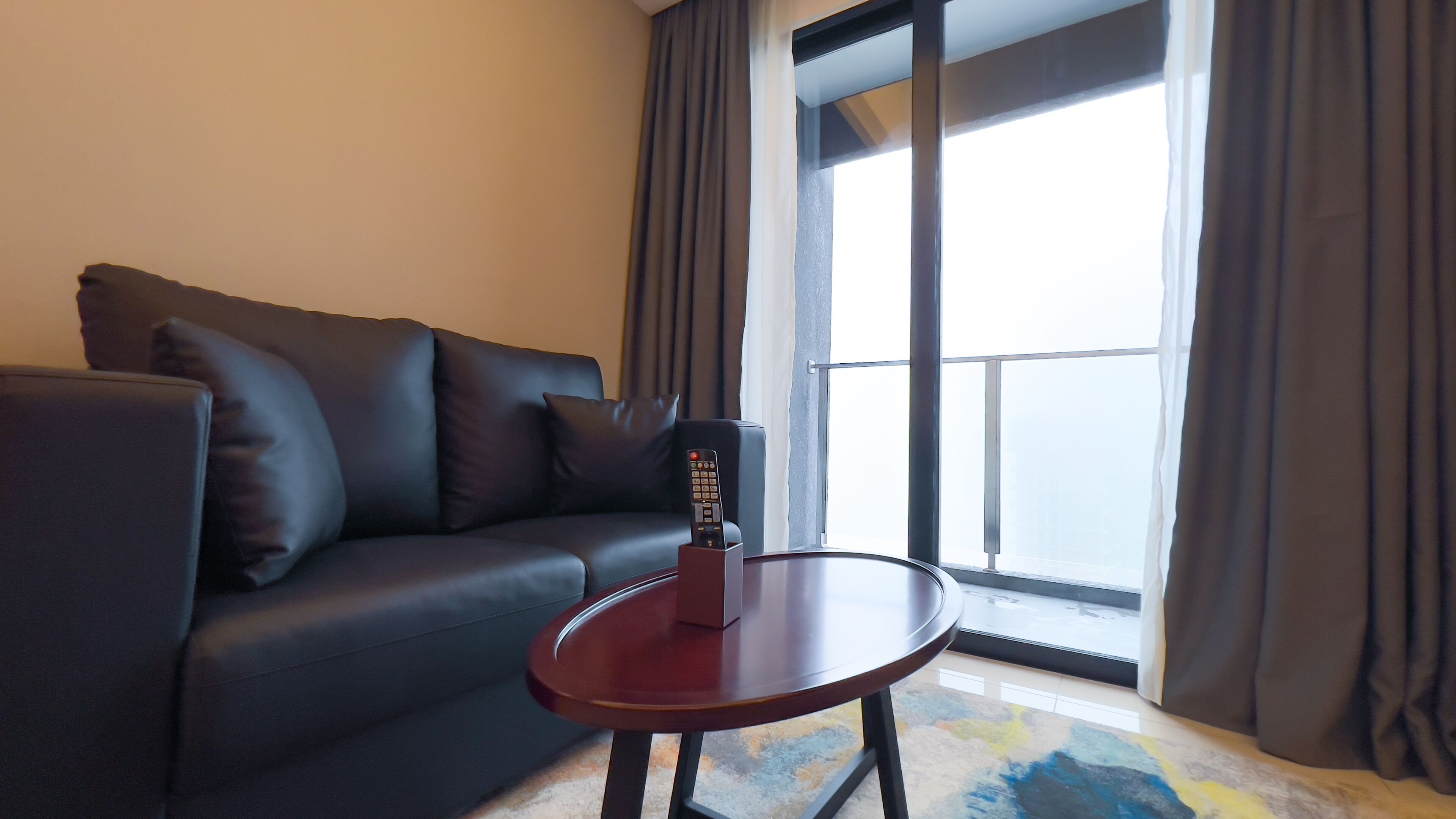 A modern living room with a dark leather sofa, a small wooden table, and a remote control on the table.