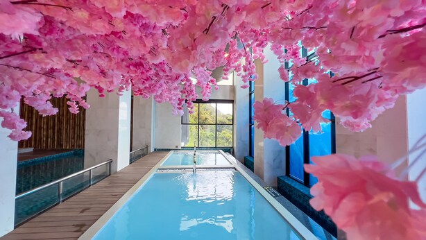 Een binnenzwembad met roze kersenbloemdecoraties erboven en uitzicht op groen buiten.